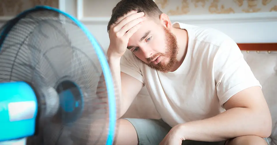 Man sits in front of a fan, trying to cool off on a hot summer day.