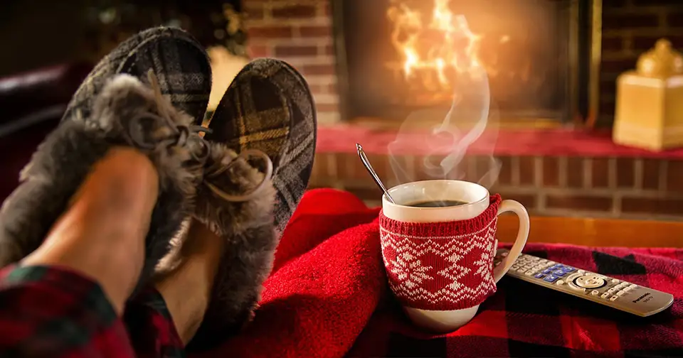 Fireplace in background, a man in comfy winter slippers drinks cocoa