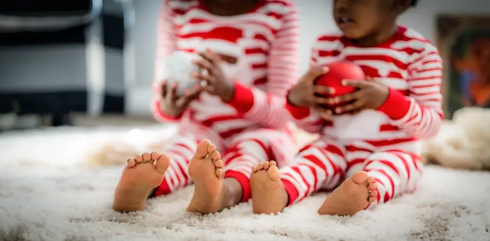 Two young children in holiday pajamas holding Christmas ornaments.